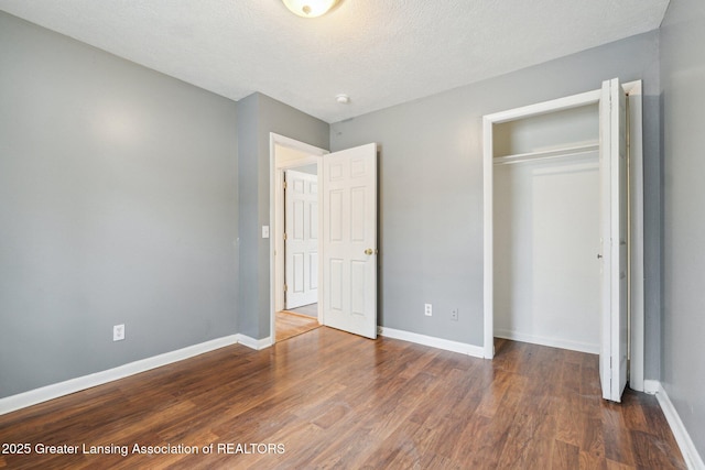 unfurnished bedroom featuring a textured ceiling, a closet, wood finished floors, and baseboards