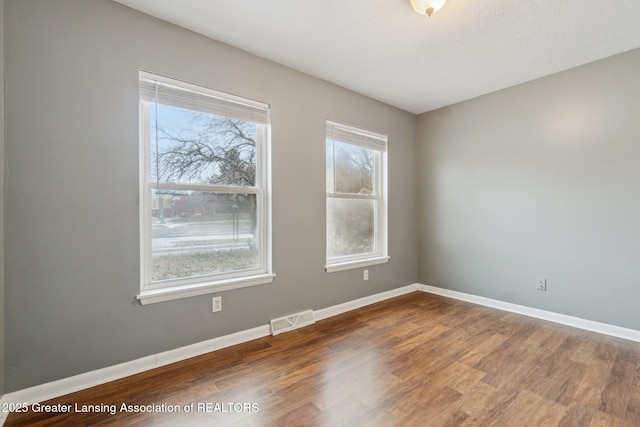 spare room with wood finished floors, visible vents, and baseboards