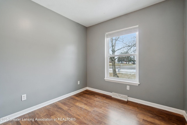 empty room with dark wood finished floors, visible vents, and baseboards