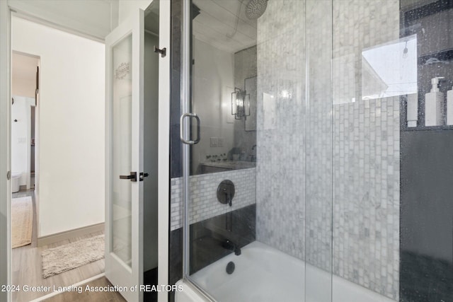 bathroom featuring wood-type flooring and shower / bath combination with glass door