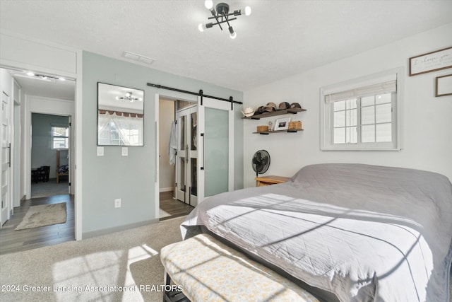 bedroom featuring a textured ceiling, multiple windows, wood-type flooring, and a barn door