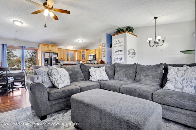 living room with ceiling fan with notable chandelier, a textured ceiling, light wood-type flooring, and lofted ceiling