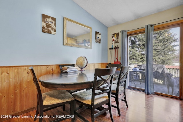 dining room featuring wood walls, hardwood / wood-style flooring, a textured ceiling, and vaulted ceiling