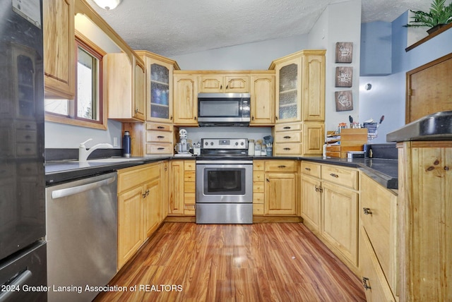 kitchen with light wood-type flooring, appliances with stainless steel finishes, a textured ceiling, sink, and vaulted ceiling