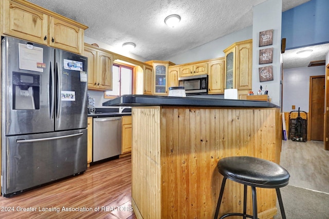 kitchen with stainless steel appliances, a breakfast bar, light wood-type flooring, and kitchen peninsula