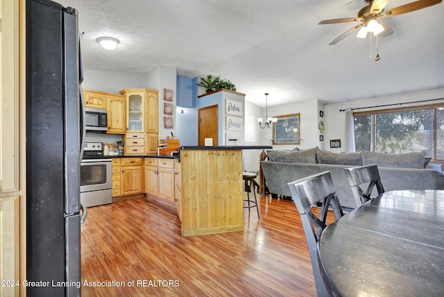 kitchen with ceiling fan with notable chandelier, stainless steel appliances, light hardwood / wood-style floors, hanging light fixtures, and a textured ceiling