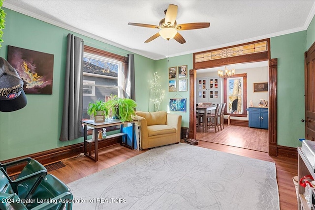 living area with a textured ceiling, hardwood / wood-style floors, ornamental molding, and ceiling fan with notable chandelier