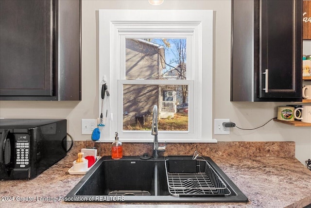 kitchen featuring light stone countertops, sink, and dark brown cabinetry