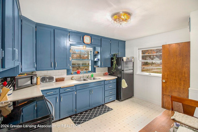 kitchen with tasteful backsplash, wooden walls, sink, blue cabinetry, and black appliances