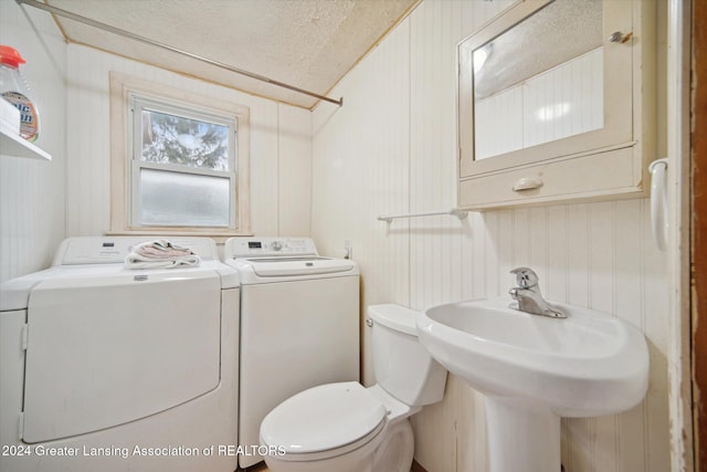 bathroom featuring wood walls, sink, toilet, a textured ceiling, and washing machine and clothes dryer