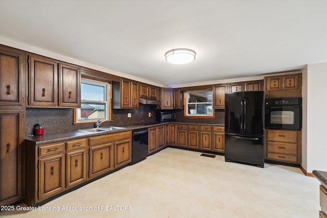 kitchen with tasteful backsplash, dark countertops, a sink, under cabinet range hood, and black appliances