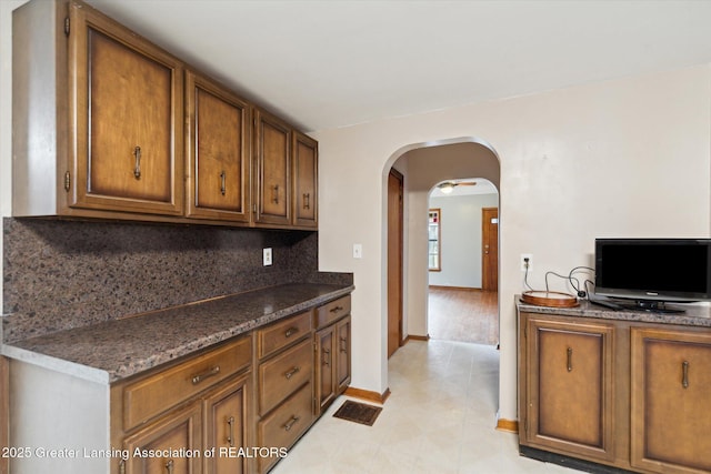 kitchen with arched walkways, baseboards, decorative backsplash, and brown cabinets