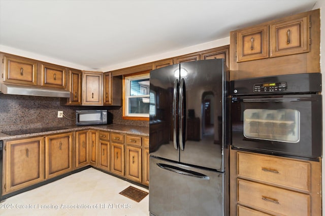 kitchen with brown cabinetry, dark countertops, under cabinet range hood, and black appliances