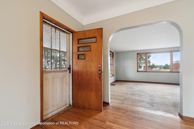 foyer with baseboards, arched walkways, and wood finished floors