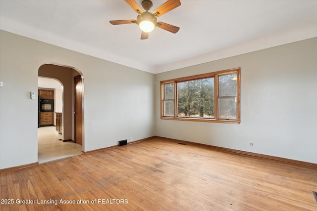 empty room with arched walkways, visible vents, light wood-style flooring, and baseboards