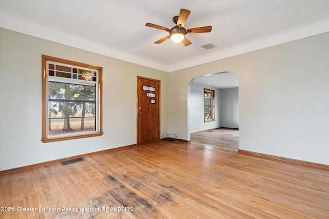 empty room with arched walkways, visible vents, ceiling fan, and light wood finished floors