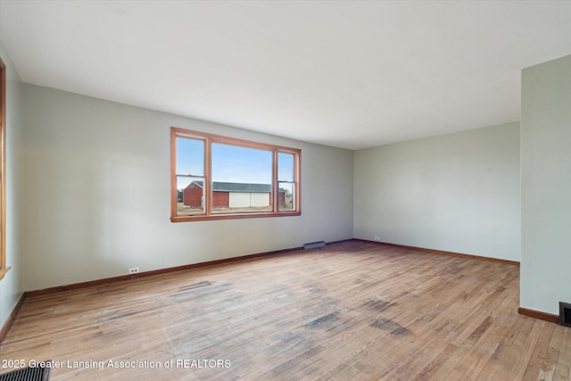 unfurnished room with wood-type flooring, visible vents, and baseboards