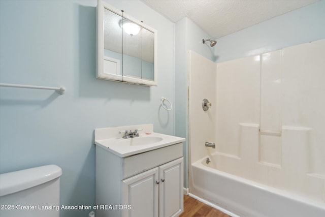 full bathroom with toilet, shower / tub combination, wood finished floors, a textured ceiling, and vanity