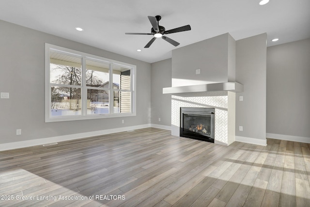 unfurnished living room with ceiling fan, a fireplace, and light hardwood / wood-style floors