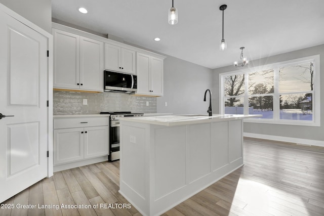 kitchen with appliances with stainless steel finishes, a kitchen island with sink, backsplash, white cabinets, and decorative light fixtures