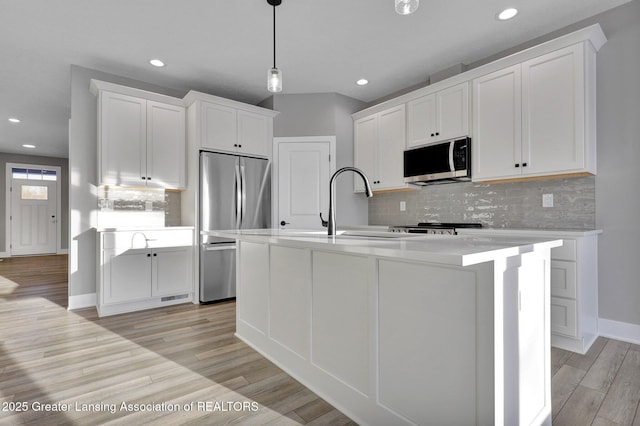 kitchen with pendant lighting, appliances with stainless steel finishes, light hardwood / wood-style flooring, and white cabinets