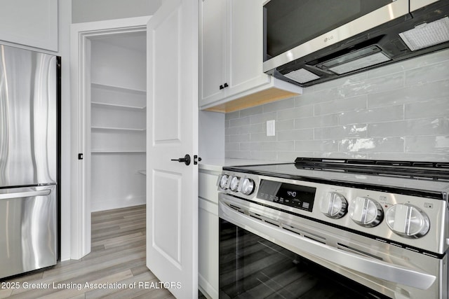 kitchen with white cabinetry, appliances with stainless steel finishes, light hardwood / wood-style floors, and backsplash