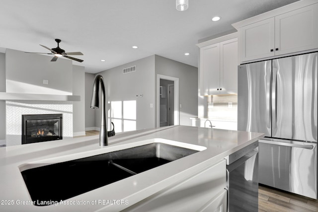 kitchen featuring sink, stainless steel fridge, a tile fireplace, dishwasher, and white cabinets