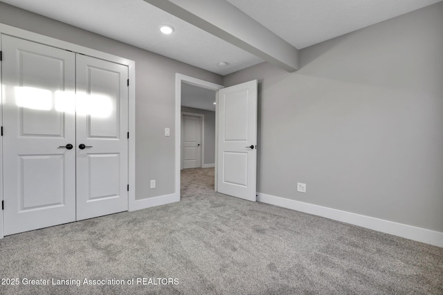 unfurnished bedroom with beamed ceiling, light colored carpet, and a closet