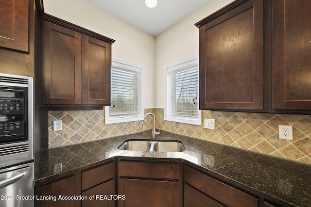 kitchen with backsplash, dark stone countertops, and sink