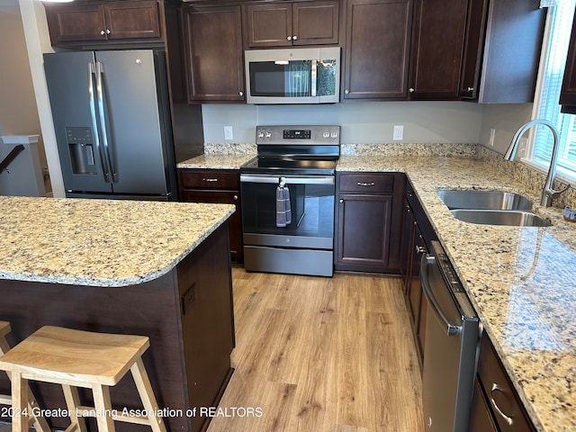 kitchen featuring light stone countertops, light wood-type flooring, stainless steel appliances, sink, and a breakfast bar area