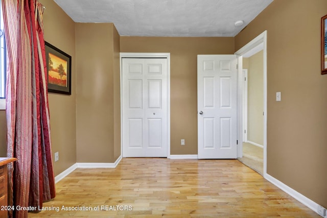 unfurnished bedroom featuring light hardwood / wood-style floors, a textured ceiling, and a closet