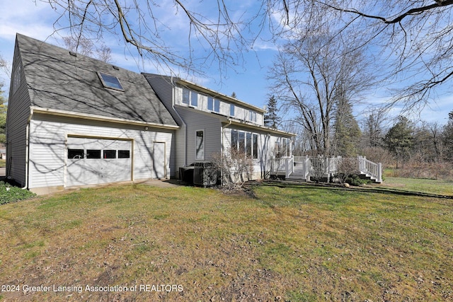 rear view of property with a yard, a garage, central AC unit, and a wooden deck