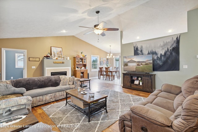 living room with lofted ceiling, light wood-type flooring, and ceiling fan with notable chandelier