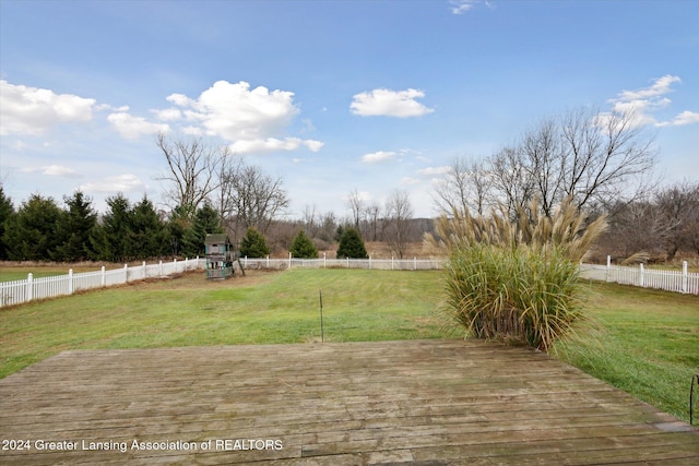 wooden terrace with a playground, a lawn, and a rural view