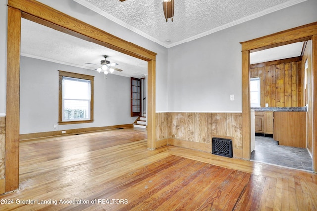 empty room featuring wood walls, light hardwood / wood-style flooring, a textured ceiling, and ornamental molding