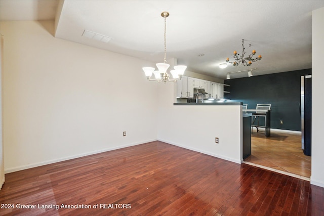 interior space with white cabinetry, dark hardwood / wood-style floors, a notable chandelier, kitchen peninsula, and decorative light fixtures