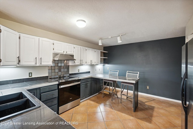 kitchen with white cabinets, light tile patterned flooring, stainless steel appliances, and a textured ceiling