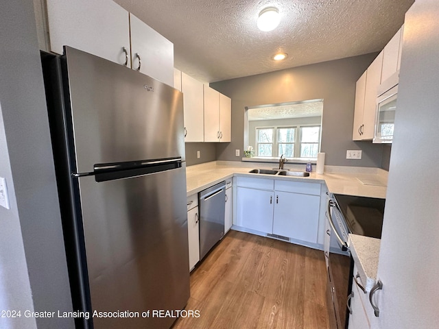 kitchen featuring light wood-type flooring, a textured ceiling, stainless steel appliances, sink, and white cabinetry