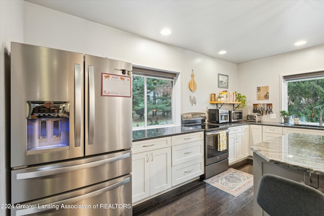 kitchen with dark stone counters, sink, dark hardwood / wood-style flooring, white cabinetry, and stainless steel appliances