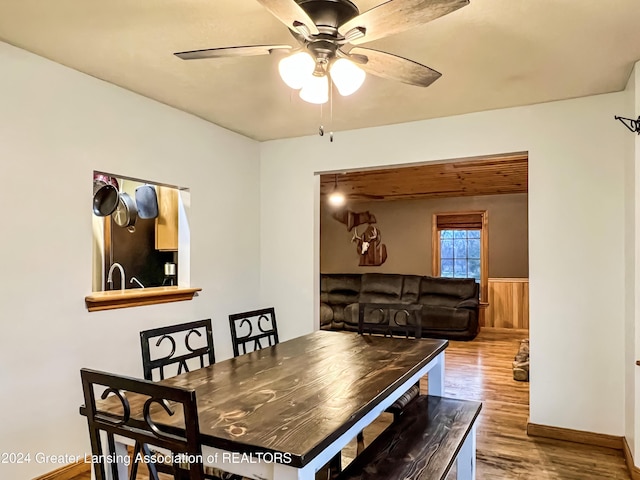 dining area featuring hardwood / wood-style flooring, ceiling fan, and wooden walls