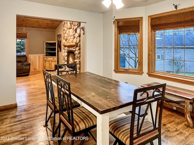 dining space featuring a stone fireplace, ceiling fan, light hardwood / wood-style flooring, and wooden walls