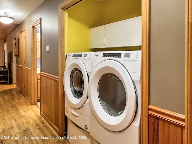 clothes washing area featuring washer and dryer, cabinets, wooden walls, and light hardwood / wood-style flooring