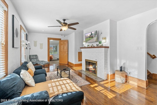 living room featuring wood-type flooring, a brick fireplace, and ceiling fan