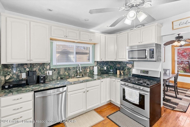 kitchen featuring backsplash, dark stone counters, white cabinets, light wood-type flooring, and stainless steel appliances