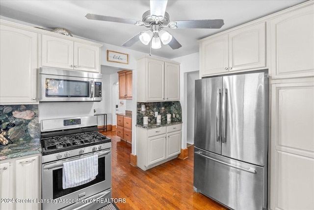 kitchen with white cabinets, dark stone countertops, appliances with stainless steel finishes, tasteful backsplash, and dark hardwood / wood-style flooring