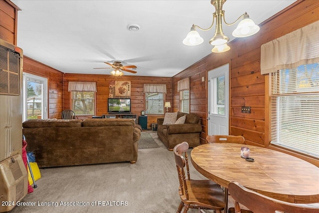 dining space with wood walls, light colored carpet, and ceiling fan with notable chandelier