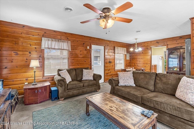 living room with carpet flooring, ceiling fan with notable chandelier, and wood walls