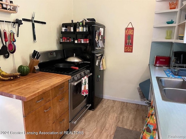 kitchen featuring gas range, light hardwood / wood-style floors, butcher block countertops, and sink