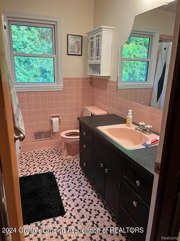 bathroom with a wealth of natural light, vanity, tile walls, and toilet