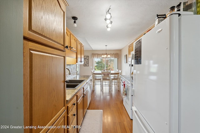 kitchen featuring white appliances, sink, hanging light fixtures, a notable chandelier, and light hardwood / wood-style floors